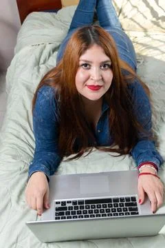 Beautiful fat model using laptop relaxed lying on her bed looking at camera Foto stock