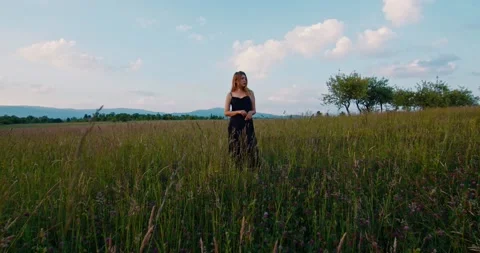 Beautiful female blonde model in long dress stands on a meadow in apple garden Stock Footage 221461663