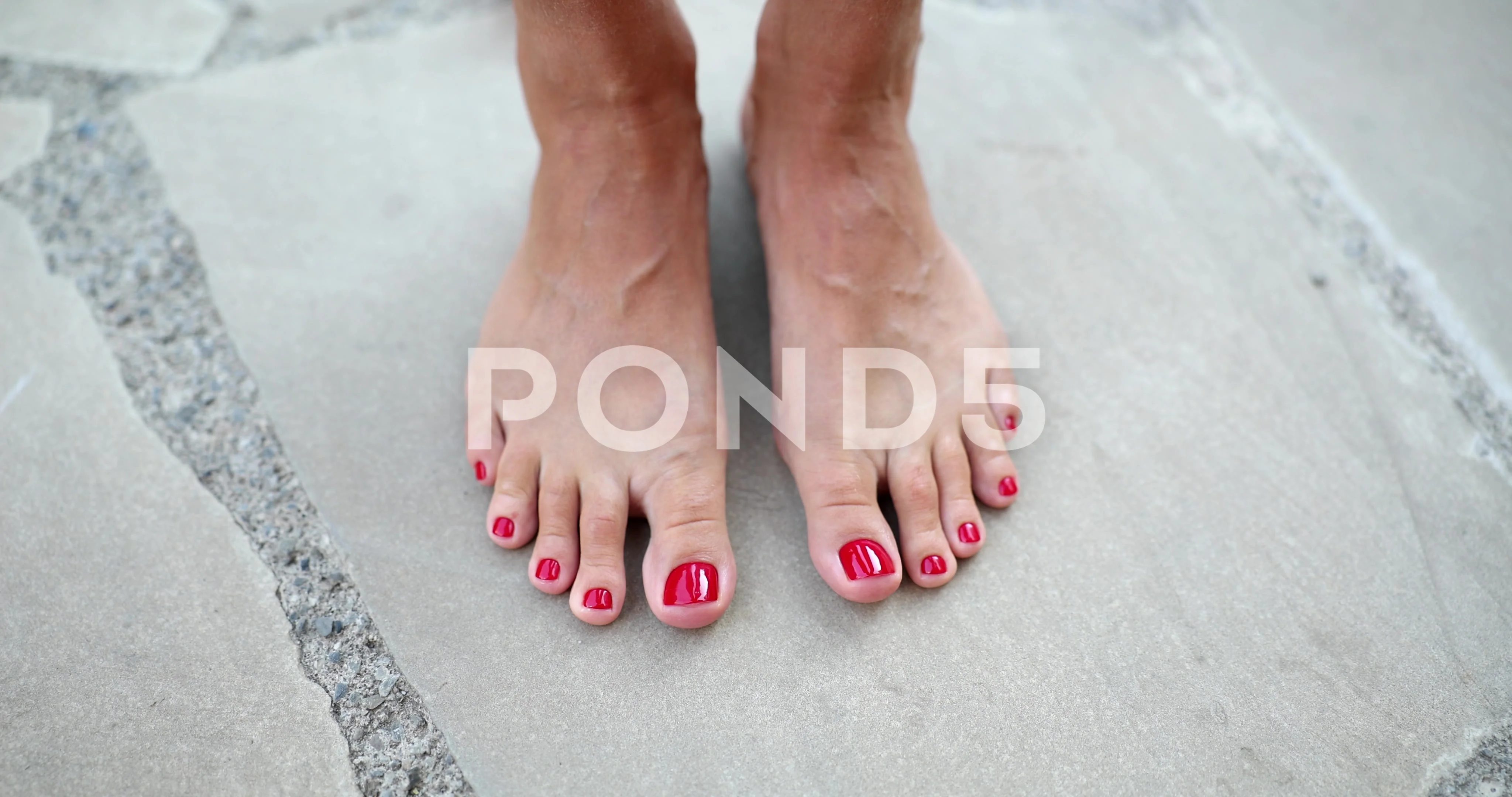 Beautiful female feet with red nails on street tiles