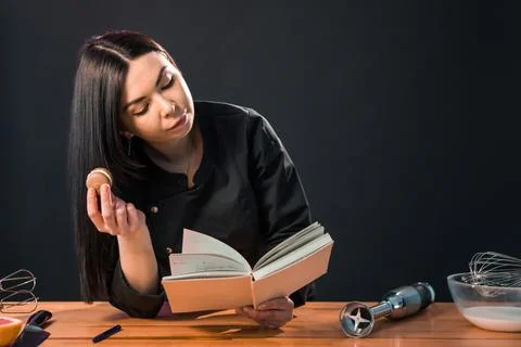 Beautiful female looking for macaroon recipe in the cook book. Stock Photos