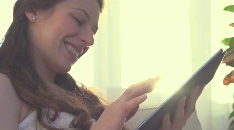 Beautiful female using PC tablet. Young wom at home sitting on sofa and chatting Stock Footage 50052706
