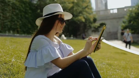 Beautiful female is working with tablet pc sitting on grass in park. Stock Footage 104313604