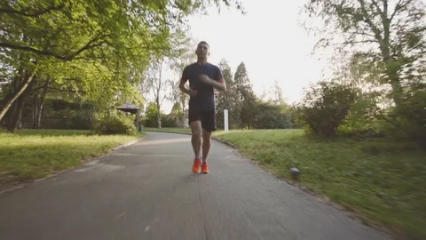 Beautiful fitness athlete man jogging outdoors in the park with sunlight Stock Footage