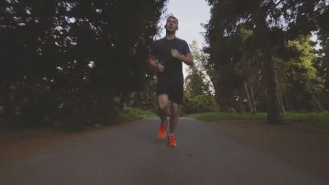 Beautiful fitness athlete man jogging outdoors in the park with sunlight Stock Footage