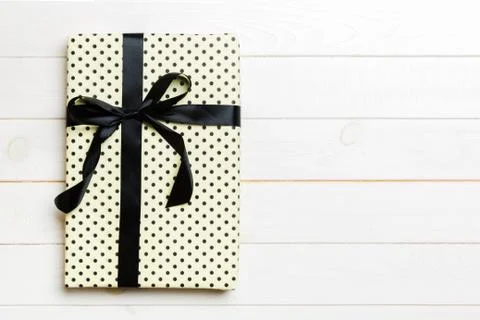Beautiful gift box with a colored bow on the white wooden table. Top view wit Stock Photos