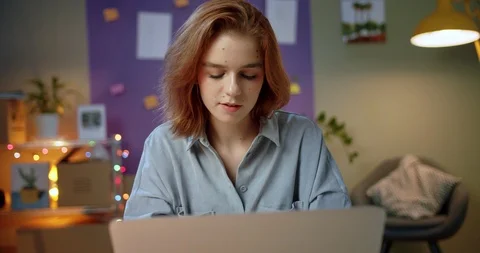 Beautiful ginger female smiling using laptop chatting online in colorful cozy Stock Footage 125314266