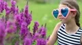 Beautiful girl in big glasses in the shape of hearts near purple flowers HD Footage