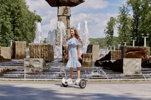 A beautiful girl in a blue dress rides a gyro scooter, hoverboard in summer. Stock Photos