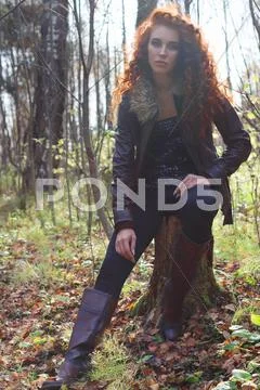 Beautiful girl in boots and jacket poses on tree stump in sunny autumn forest Stock Photos