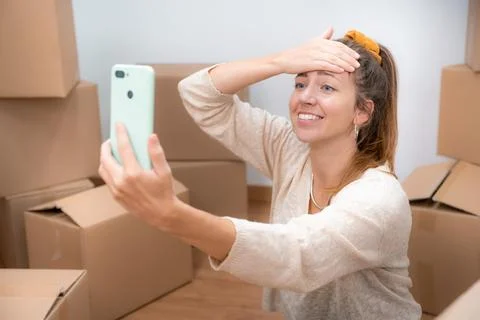 Beautiful girl with cardboard boxes unpacking in new home taking a selfie or Stock Photos