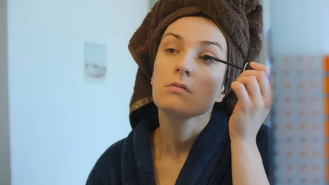 Beautiful girl doing make up put cosmetics on face looking in mirror in bathroom Vidéo 128608981