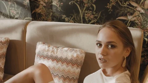 Beautiful girl with earrings posing while sitting on the couch Video stock 81306596