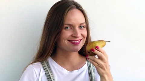 Beautiful girl eats ripe pear on white background. Stock Footage 80583282