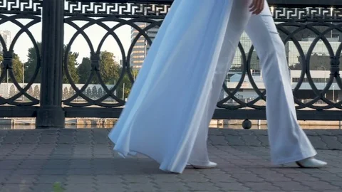 A beautiful girl with long hair in white clothes is walking along the city Stock Footage