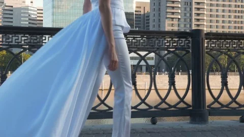 A beautiful girl with long hair in white clothes is walking along the city Stock Footage