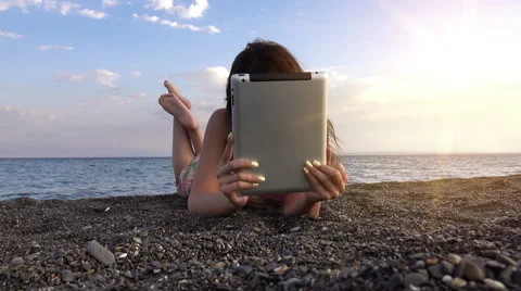 Beautiful girl looking at tablet in the beach at sunset with sunshine Stock Footage 68002853