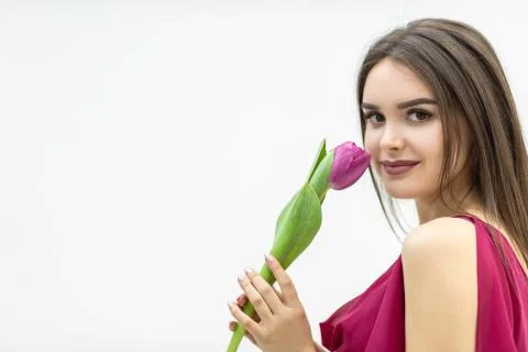 Beautiful girl in the maroon dress smells atender tulip over white background. Stock Photos