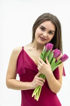 Beautiful girl in the maroon dress smells atender tulip over white background. Stock Photos