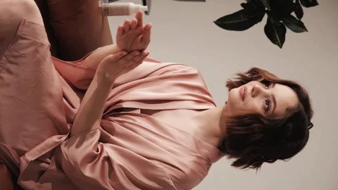 Beautiful girl in a pink silk bathrobe posing in a home interior with hand cream Stock Footage 244680853