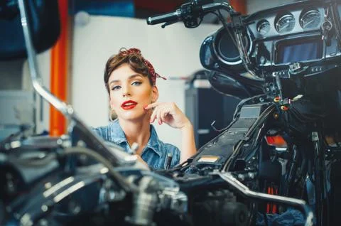 Beautiful girl posing repairs a motorcycle in a workshop, pin-up style, servi Stock Photos