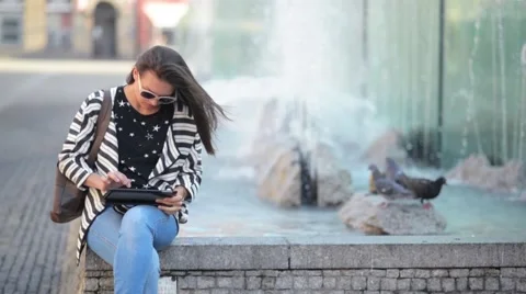 Beautiful Girl reading and browsing an ebook or a tablet sitting in a bench at Stock Footage