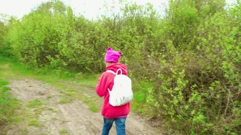Beautiful girl in a red jacket with a backpack goes on the overgrown forest r Stock Footage 127713951
