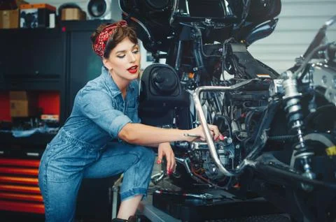 Beautiful girl repairs a motorcycle in a workshop, pin-up style, service and  Stock Photos