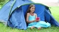 Beautiful girl sits on grass near tourist tent and communicates via smartphone HD Footage