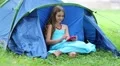 Beautiful girl sits on grass near tourist tent and uses smartphone HD Footage
