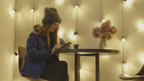 A beautiful girl sits at a table in a cafe and uses the phone Stock Footage 264657953
