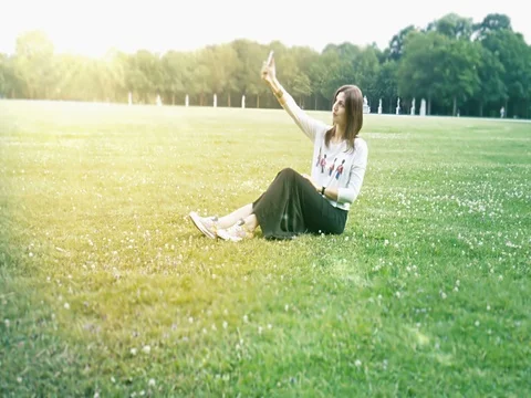 Beautiful girl sitting on lawn and making selfie on smartphone Stock Footage