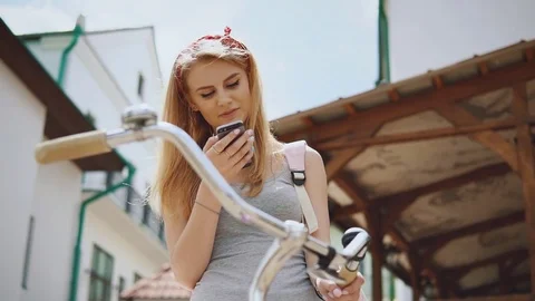 Beautiful girl standing in the street with a bike use phone and smiling Stock Footage