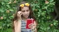 Beautiful girl stands near apple tree and speaks on red smartphone HD Footage