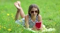 Beautiful girl in sunglasses with red smartphone lies on green grass HD Footage