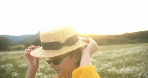 Beautiful girl in sunglasses at sunset puts on straw hat Stock Footage 111961553