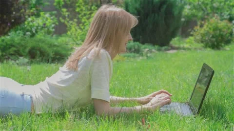 Beautiful girl using Notebook laying on grass in park 1 Stock Footage 64706870