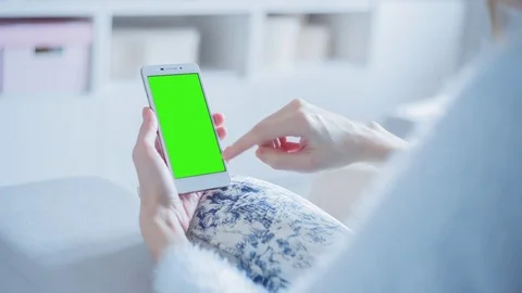 Beautiful girl using SmartPhone with pre keyed green screen sitting on sofa Stock Footage 73206479