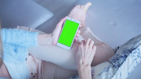 Beautiful girl using SmartPhone with pre keyed green screen sitting on sofa Stock Footage 73321116