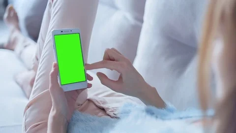 Beautiful girl using SmartPhone with pre keyed green screen laying on sofa Stock Footage 73370990