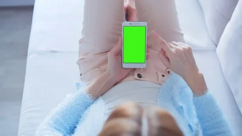 Beautiful girl using SmartPhone with pre keyed green screen laying on sofa Stock Footage 73374409