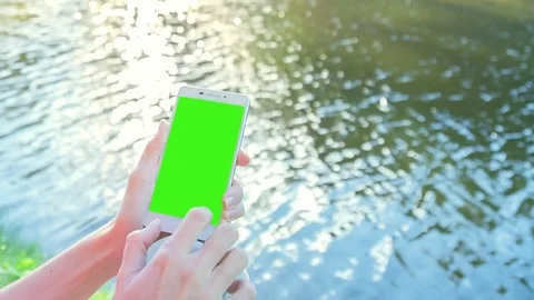 Beautiful Girl Using SmartPhone with pre-keyed green screen Sitting Near Lake Stock Footage 73754962