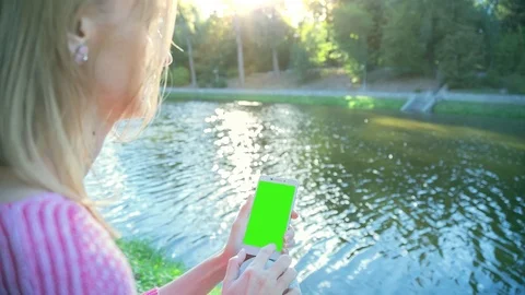 Beautiful Girl Using SmartPhone with pre-keyed green screen Sitting Near Lake 1 Stock Footage 73755995