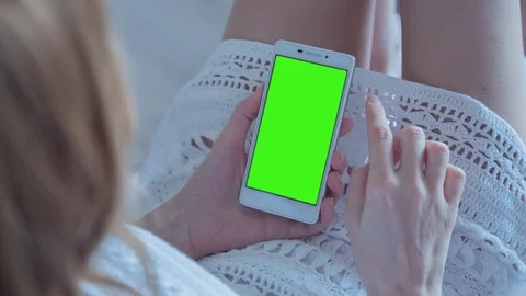 Beautiful girl using SmartPhone with pre-keyed green screen laying on sofa Stock Footage 74416319
