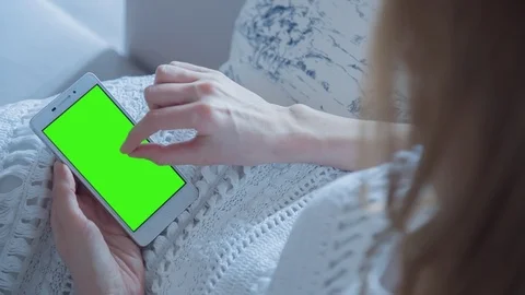 Beautiful girl using SmartPhone with pre-keyed green screen laying on sofa Stock Footage 74488973