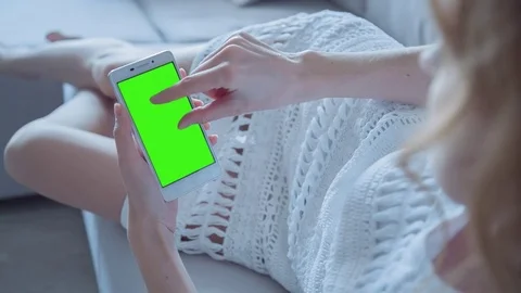 Beautiful girl using SmartPhone with pre-keyed green screen laying on sofa Stock Footage 74490880