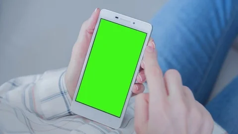 Beautiful girl using SmartPhone with pre-keyed green screen laying on sofa Stock Footage 74897100