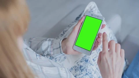 Beautiful girl using SmartPhone with pre-keyed green screen sitting on sofa Stock Footage 75019780