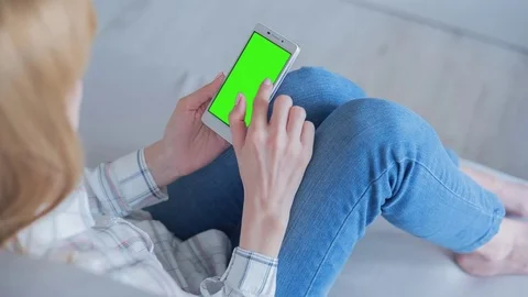 Beautiful girl using SmartPhone with pre-keyed green screen sitting on sofa Video stock 75379844