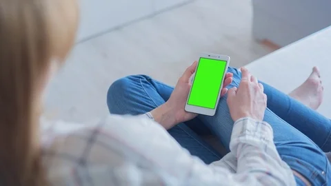 Beautiful girl using SmartPhone with pre-keyed green screen laying on sofa Video stock 75453560