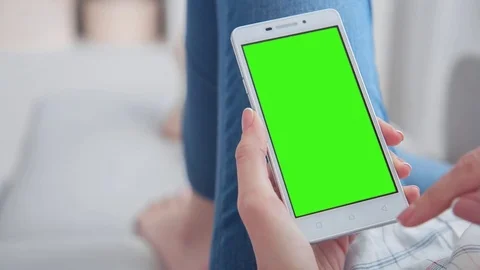Beautiful girl using SmartPhone with pre-keyed green screen laying on sofa at Stock Footage 79505380